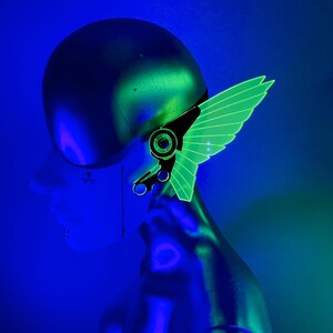 May include: A green and black ear cuff with a wing design. The ear cuff is made of acrylic and is designed to be worn on the upper ear.