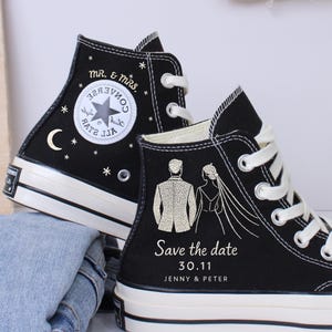 May include: Black high-top sneakers with white laces and soles. One shoe features a star and moon design with "Mr. & Mrs." text. The other shoe has a bride and groom graphic with "Save the date 30.11 Jenny & Peter" text.