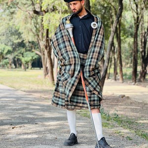 Peut inclure: Un b&eacute;ret noir, une chemise noire boutonn&eacute;e et un kilt &agrave; carreaux dans des tons de beige, vert et noir. La tenue comprend un ch&acirc;le &agrave; carreaux assorti drap&eacute; sur les &eacute;paules, des chaussettes blanches hautes, des baskets noires et une masse.