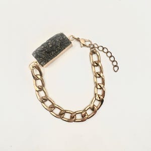 May include: A gold chain bracelet with a dark gray rectangular stone pendant.