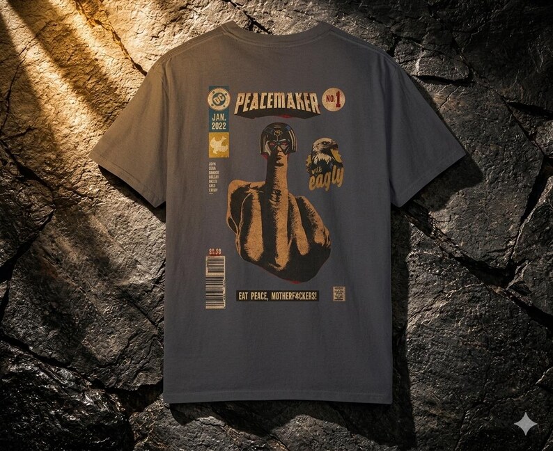 May include: Dark gray t-shirt with a comic book style graphic on the back. The graphic features a figure giving the middle finger, with text that reads "PEACEMAKER" and "EAT PEACE, MOTHERFUCKERS!"