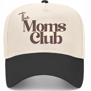 Peut inclure: Casquette de baseball avec une couronne cr&egrave;me et une visi&egrave;re noire. Le texte "The Moms Club" est inscrit en lettres marron sur le devant. La casquette a une visi&egrave;re incurv&eacute;e et un bouton sur le dessus.