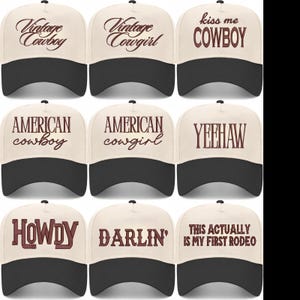 May include: Nine baseball caps with a cream-colored crown and a black brim. Each cap features text in a brown, western-style font. The phrases include "Vintage Cowboy," "Kiss Me Cowboy," and "This Actually Is My First Rodeo."
