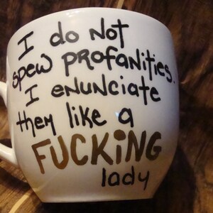 May include: White ceramic mug with black and brown handwritten text. The text reads "I do not spew profanities. I enunciate them like a FUCKING lady."