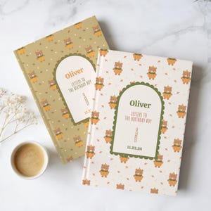 Könnte beinhalten: Zwei Hardcover-Bücher mit einem wiederkehrenden Muster aus Bären in Kürbiskostümen. Das linke Buch hat einen beigen Einband, das rechte ist cremefarben. Beide zeigen ein zentrales Etikett mit dem Text Oliver, Letters to the Birthday Boy.
