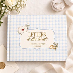 Könnte beinhalten: Ein rechteckiges Gästebuch mit einem hellblau-weiß karierten Einband. In der Mitte befindet sich ein cremefarbenes Etikett mit dem goldenen Text "LETTERS to the bride", "MADISON CARTER" und "05.12.2027", verziert mit einem Umschlag und Goldringen.