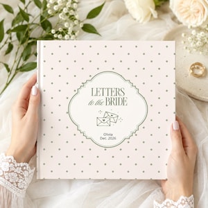 Puede incluir: Un libro cuadrado con cubierta rosa claro que presenta un patrón de pequeños puntos verde salvia. El centro muestra un marco decorativo verde salvia con el texto "LETTERS to the BRIDE", dos iconos de sobres, el nombre "Olivia" y "Dec. 2026".