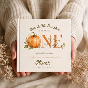 Könnte beinhalten: Ein quadratisches Hardcover-Buch mit cremefarbenem Einband und einer Aquarell-Illustration eines Kürbisses. Der Text lautet Our Little Pumpkin IS TURNING ONE, LETTERS TO THE BIRTHDAY CHILD, der Name Oliver und das Datum 10.10.2026 in Braun und Orange.