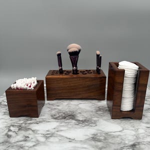 May include: Three wooden organizers for bathroom essentials. The largest organizer has a row of holes for storing makeup brushes. The middle organizer holds cotton swabs. The smallest organizer holds cotton rounds.