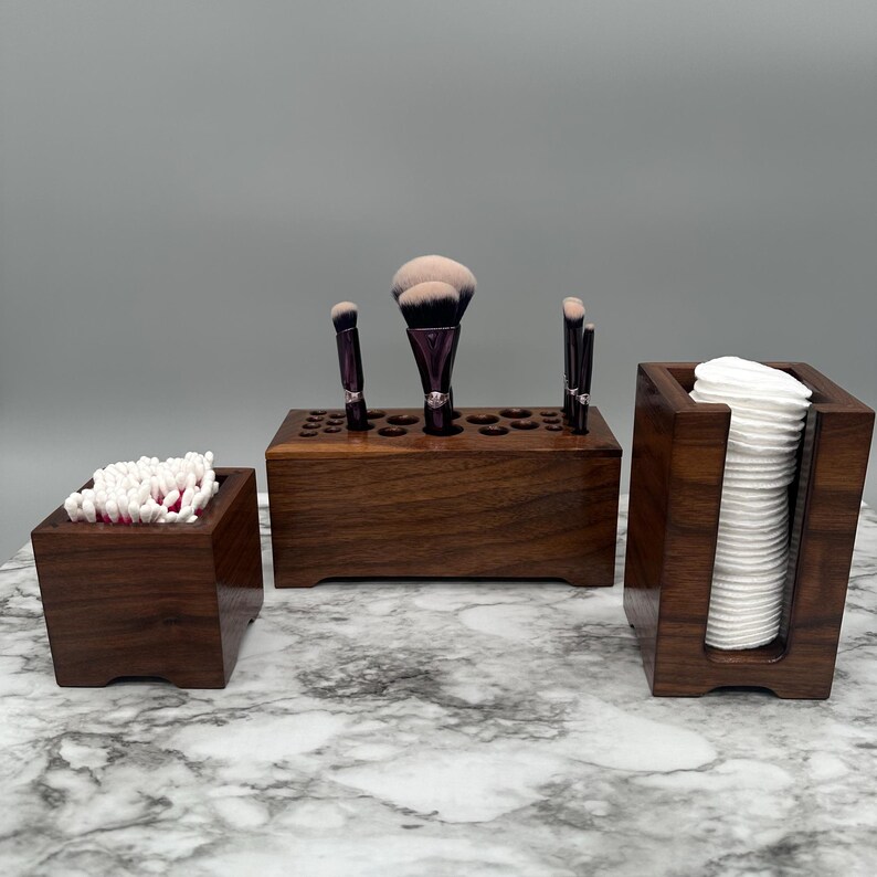 May include: Three wooden organizers for bathroom essentials. The largest organizer has a row of holes for storing makeup brushes. The middle organizer holds cotton swabs. The smallest organizer holds cotton rounds.