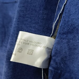 Peut inclure: Gros plan sur une section de tissu en daim bleu fonc&eacute;. Une &eacute;tiquette blanche avec du texte et des symboles d'entretien est visible. Le tissu a un aspect doux et textur&eacute;.