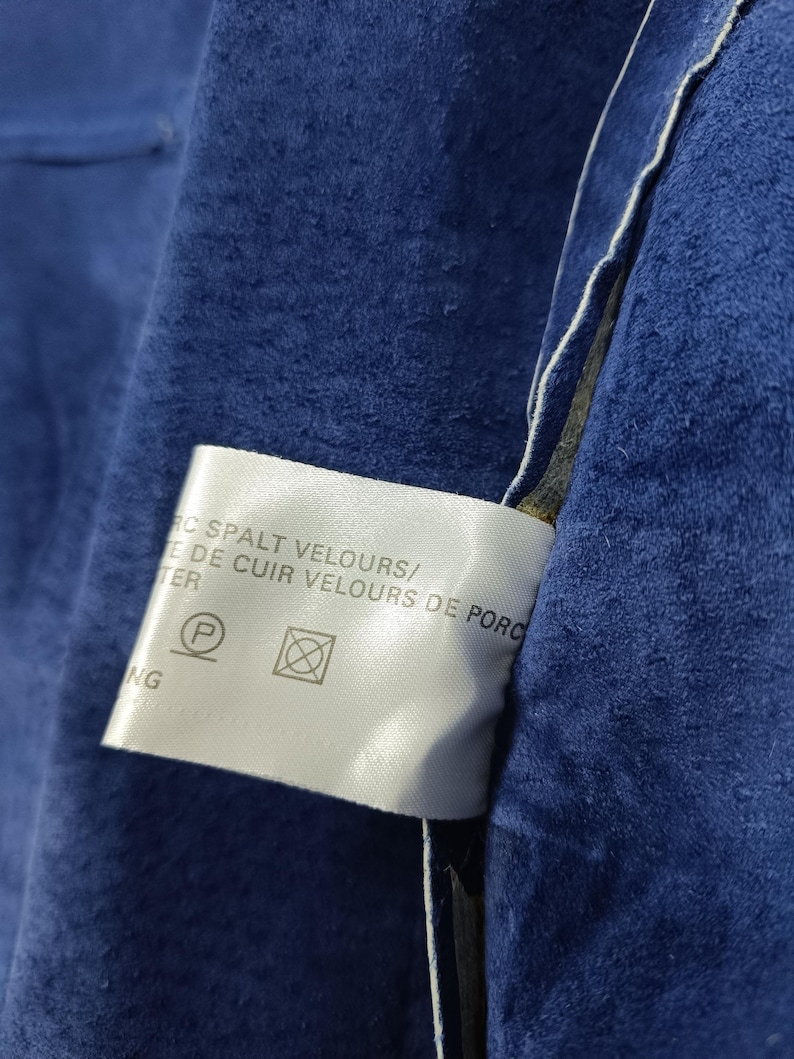 Peut inclure: Gros plan sur une section de tissu en daim bleu fonc&eacute;. Une &eacute;tiquette blanche avec du texte et des symboles d'entretien est visible. Le tissu a un aspect doux et textur&eacute;.