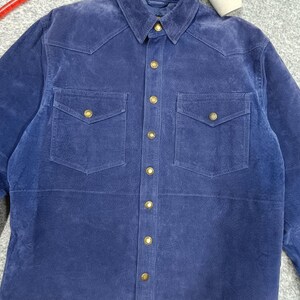 Peut inclure: Une chemise en daim bleu marine avec deux poches de poitrine et des boutons dor&eacute;s. La chemise a un col classique et une fermeture boutonn&eacute;e sur le devant. Le tissu a une texture douce et velout&eacute;e. Cette chemise est un ajout &eacute;l&eacute;gant &agrave; toute garde-robe.