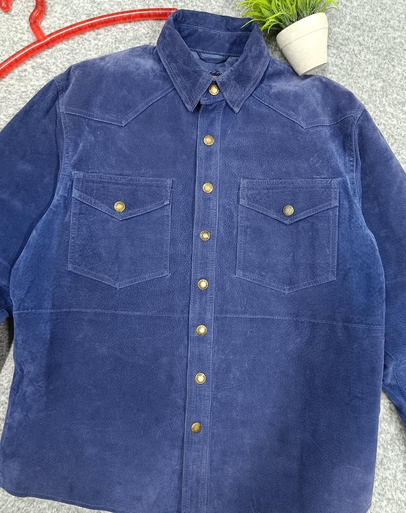 Peut inclure: Une chemise en daim bleu marine avec deux poches de poitrine et des boutons dor&eacute;s. La chemise a un col classique et une fermeture boutonn&eacute;e sur le devant. Le tissu a une texture douce et velout&eacute;e. Cette chemise est un ajout &eacute;l&eacute;gant &agrave; toute garde-robe.