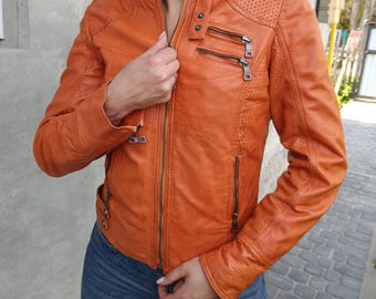 Peut inclure: Veste en cuir orange avec fermeture éclair, deux poches zippées et coutures décoratives. La veste a un col montant et des détails perforés sur les épaules. Les manches sont longues et ajustées.