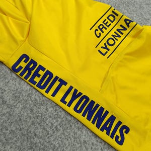 Puede incluir: Camiseta deportiva amarilla brillante con la inscripci&oacute;n "CREDIT LYONNAIS" en azul marino. La camiseta tiene un bolsillo y el texto se repite en la manga. La tela parece ser un material ligero y transpirable.