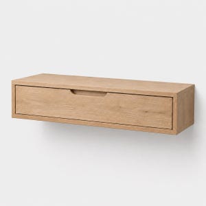 Peut inclure: Tiroir flottant rectangulaire en bois clair avec une poignée encastrée. Le tiroir est fixé à un mur blanc. Le design est minimaliste et moderne, adapté au rangement dans une chambre ou un salon.
