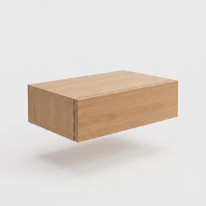May include: A rectangular wall-mounted floating shelf unit crafted from light-toned oak wood. The piece features a clean, boxy design with a smooth, natural wood grain finish, a flat top surface, and a solid front panel with no visible hardware.