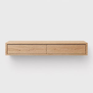 Peut inclure: Un meuble mural flottant en bois avec deux tiroirs. Le meuble est en bois de couleur claire et présente un design minimaliste. Les tiroirs sont rectangulaires et ont une surface lisse et plate. Le meuble est fixé sur un mur blanc.