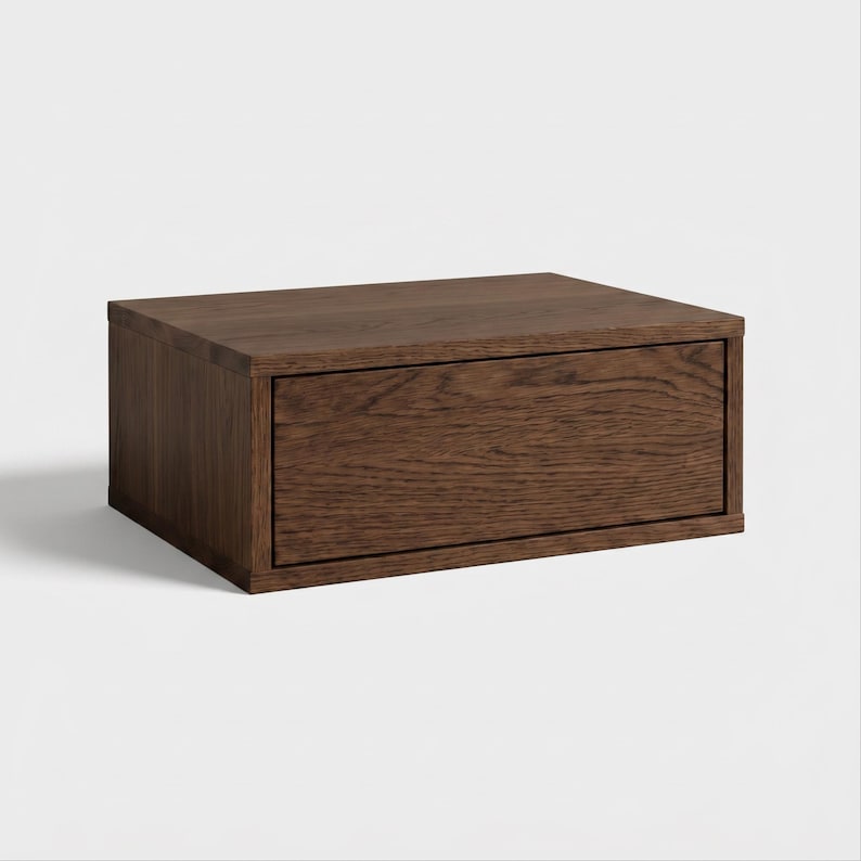 May include: A rectangular storage box crafted from dark brown wood with a visible natural grain pattern. The box features a single front-facing drawer panel that is flush with the frame, creating a clean and simple box-like structure.