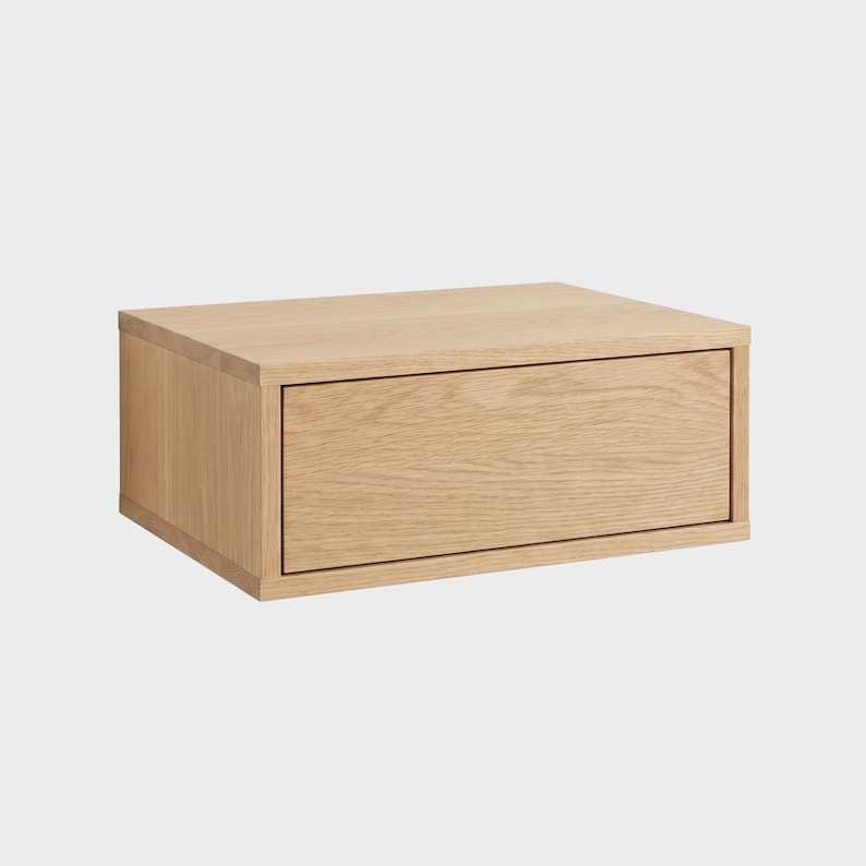 May include: A rectangular wall-mounted storage unit crafted from light-toned wood with a visible grain pattern. The unit features a single front-facing drawer with a clean, flat surface and a simple frame construction, presented against a plain background.