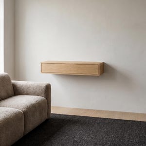 Könnte beinhalten: Ein rechteckiges, helles Holz-Wandregal mit einer einzelnen horizontalen Schublade. Das Möbelstück ist direkt an einer schlichten Wand montiert und bietet eine klare, lineare Aufbewahrungslösung mit einer glatten, natürlichen Holzmaserung ohne sichtbare Beschläge.