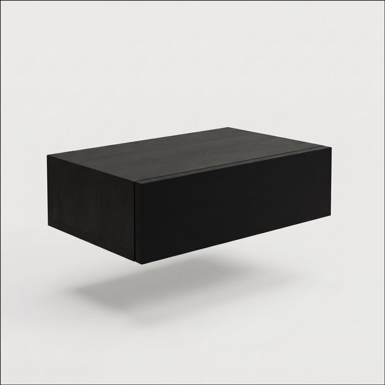 May include: A rectangular floating wall shelf with a dark black wood grain finish. The unit features a clean, boxy design with a flat top surface and a solid front panel, presenting a simple, functional storage solution for mounting on a wall.
