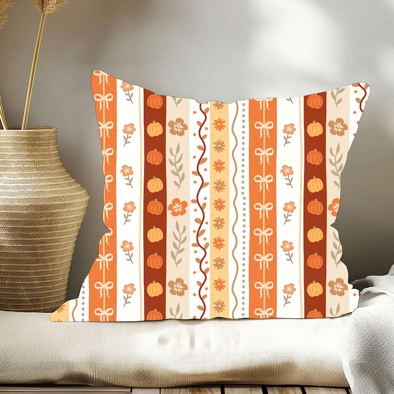 May include: Square decorative pillow with a fall-themed pattern. The design features vertical stripes in orange, white, and brown, adorned with pumpkins, flowers, bows, and leaves. The pillow is likely used for home decor.