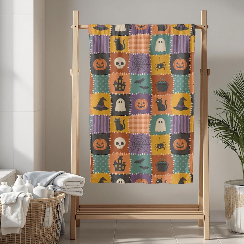 Op de afbeelding: Een rechthoekige handdoek met een patchworkpatroon van vierkanten met een Halloween-thema. Het ontwerp bevat illustraties van oranje pompoenen, zwarte katten, witte geesten, schedels, spinnenwebben, vleermuizen, heksenhoeden en ketels.