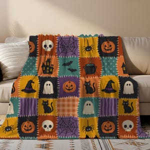 Op de afbeelding: Een fleece deken met een patchwork ontwerp van Halloween iconen, waaronder oranje pompoenen, witte schedels, zwarte katten, geesten, spinnen, webben, vleermuizen, een spookhuis en een zwarte ketel, gescheiden door witte stiksel-achtige lijnen.