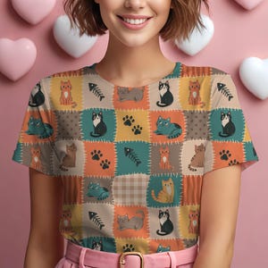 May include: A short-sleeved t-shirt featuring a patchwork-style print of various cats, fish bones, and paw prints in shades of orange, teal, brown, and cream. The design includes stitched-look borders between the colorful rectangular sections.