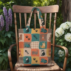 May include: A tote bag featuring a patchwork design of various colored squares. The pattern includes illustrations of cats in different poses, fish skeletons, and paw prints in shades of orange, teal, beige, and brown with white stitching.