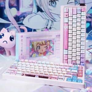 May include: A mechanical keyboard with a light pink frame and a mix of white, pink, and translucent blue keycaps. The keyboard features custom graphic prints on several keys. A matching keyboard box with anime-style artwork is positioned behind it.