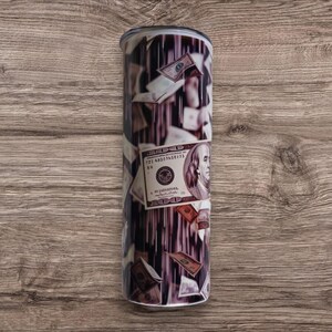 May include: A stainless steel tumbler with a design of falling US dollar bills. The bills are in various denominations and feature the portrait of Benjamin Franklin.