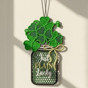 May include: Embroidered St. Patrick's Day decoration featuring a green jar filled with shamrocks and the text "Just Plain Lucky." The jar has a black outline, a white and black striped lid, and a gold bow.