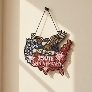 May include: A patriotic wall hanging in the shape of the United States, celebrating the 250th anniversary. Features an eagle, stars, and stripes design with the years 1776-2026. The hanging is suspended by a black string.