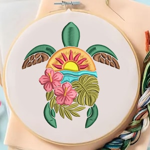May include: Embroidered turtle design in a wooden hoop. The turtle features a sunset, ocean, and hibiscus flowers. The design is in shades of green, brown, yellow, pink, and blue. Embroidery floss and pink scissors are visible.