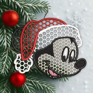 May include: A Christmas ornament featuring a stylized Mickey Mouse head wearing a Santa hat. The ornament has a honeycomb pattern and is red, black, white, and beige. Two red Christmas balls and a pine branch are in the background.