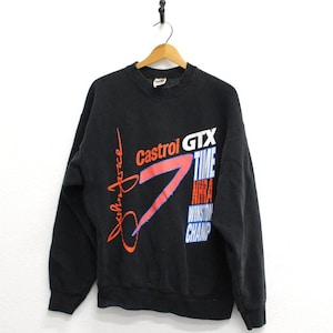May include: Black crew neck sweatshirt with the text "John Force" in red script and "Castrol GTX" in orange and white. The sweatshirt also features a large red and blue graphic and the words "TIME NHRA Winston CHAMP".