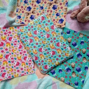 May include: Three rectangular protective cases for electronic tablets, each featuring a repeating pattern of colourful boba tea drinks and small floral elements. The cases are displayed in light pink, bright turquoise, and soft peach colourways.