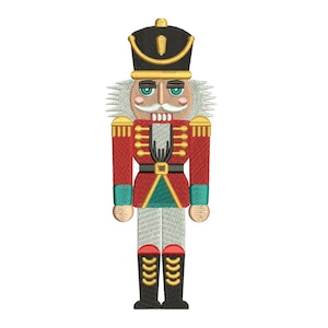 May include: Embroidered image of a traditional nutcracker soldier. The nutcracker is dressed in a red jacket with gold trim, a black hat, and white trousers. The design includes details like a mustache, eyebrows, and boots. The overall design is a festive, holiday theme.