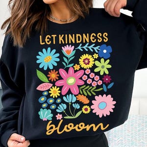 May include: Black sweatshirt with a colorful floral design and the text "Let Kindness Bloom" in yellow.