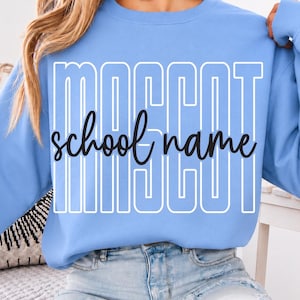 May include: A light blue long-sleeve sweatshirt featuring the word MASCOT in large white outlined block letters with the words school name written in a black cursive script font layered horizontally across the center of the design.