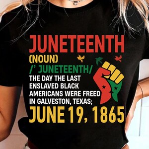 May include: A black t-shirt featuring a graphic design with the text JUNETEENTH (NOUN) /' JUNETEENTH/ THE DAY THE LAST ENSLAVED BLACK AMERICANS WERE FREED IN GALVESTON, TEXAS; JUNE 19, 1865. A raised fist icon in red, yellow, and green is included.