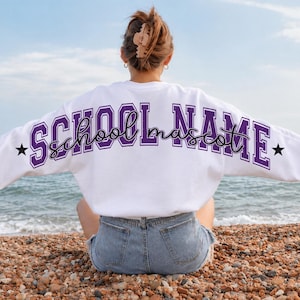 May include: A white long-sleeve sweatshirt featuring the text SCHOOL NAME in purple block letters with a black outline, and the word school mascot in a black cursive script, accented by two black stars on the sides of the back design.