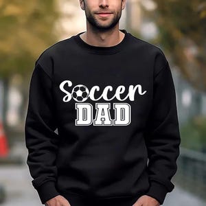 May include: Black sweatshirt with white text that reads "Soccer Dad" and a white soccer ball graphic.