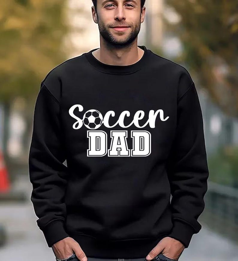 May include: Black sweatshirt with white text that reads "Soccer Dad" and a white soccer ball graphic.
