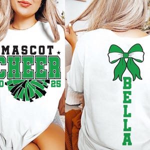 May include: White t-shirt with green and black cheerleading design on the front and a green bow with the name "BELLA" on the back. The text on the front says "MASCOT CHEER 20 25".