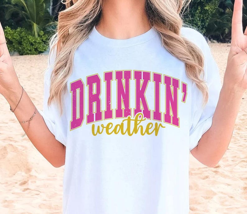 May include: White t-shirt with the text "DRINKIN' weather" in pink and gold letters.