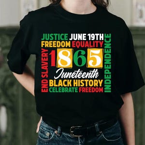 May include: Black t-shirt with a colorful graphic design celebrating Juneteenth. The design includes the text "Justice, Freedom, Equality, Independence, End Slavery, Black History, Celebrate Freedom" and the year "1865".